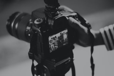 黒のデジタル一眼レフ カメラを持っている人のグレースケール写真
