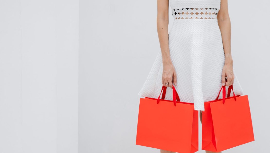 crop unrecognizable woman carrying red shopping bags in studio